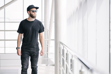 Hipster handsome male model with beard wearing black blank t-shirt with space for your logo or design in casual urban style