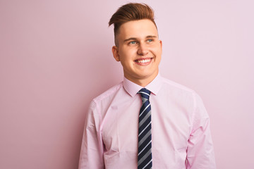 Young handsome businessman wearing shirt and tie standing over isolated pink background looking away to side with smile on face, natural expression. Laughing confident.
