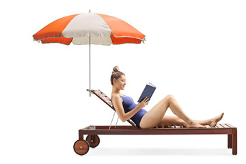Young woman reading a book and relaxing on a sunbed under umbrella