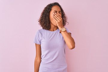 Young brazilian woman wearing t-shirt standing over isolated pink background bored yawning tired covering mouth with hand. Restless and sleepiness.