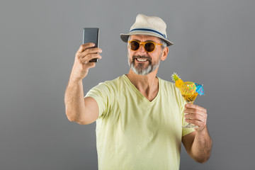 portrait of middle aged man summer dressed drinking cocktail and taking picture with his cellphone