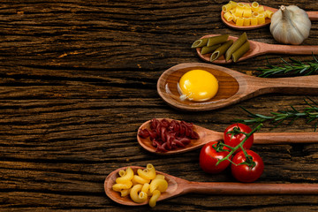 Different pasta types in wooden spoons on the table. Top view. Space for text. Old wooden background.