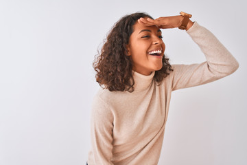 Young brazilian woman wearing turtleneck sweater standing over isolated white background very happy and smiling looking far away with hand over head. Searching concept.
