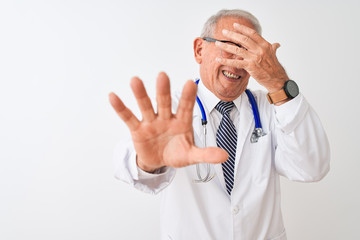 Senior grey-haired doctor man wearing stethoscope standing over isolated white background covering eyes with hands and doing stop gesture with sad and fear expression. Embarrassed and negative 