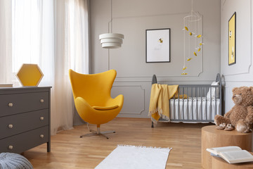 Trendy yellow egg chair in elegant grey nursery with wooden crib and posters on the wall - obrazy, fototapety, plakaty