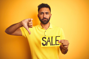 Young arab indian hispanic man holding sale banner over isolated yellow background with angry face,...