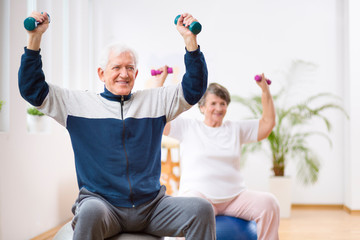 Fototapeta na wymiar Elderly man and woman exercising on gymnastic balls during physiotherapy session at hospital