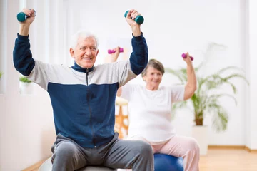 Fototapete Elderly man and woman exercising on gymnastic balls during physiotherapy session at hospital © Photographee.eu