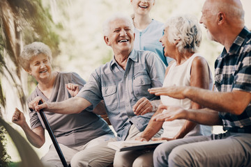Happy elderly man with walking stick and smiling senior people relaxing in the garden