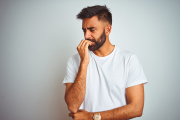 Fototapeta na wymiar Young indian man wearing t-shirt standing over isolated white background looking stressed and nervous with hands on mouth biting nails. Anxiety problem.