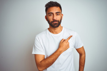 Young indian man wearing t-shirt standing over isolated white background Pointing with hand finger...