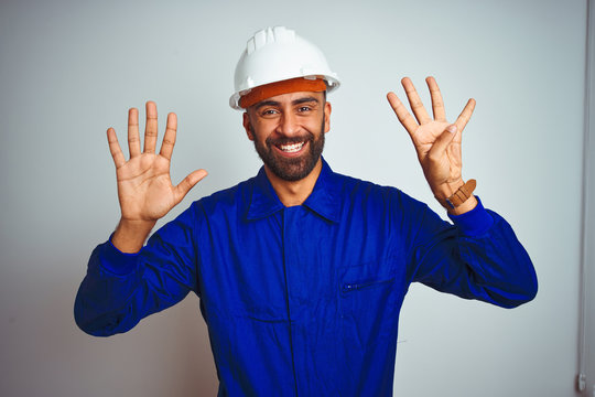 Handsome indian worker man wearing uniform and helmet over isolated white background showing and pointing up with fingers number nine while smiling confident and happy.