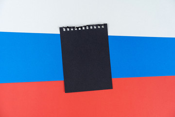 Blacklist Russia. Mourning, ban, sanctions, politics. black sheet of notepad is on Russian flag. Mock up, copy space, pattern, cardboard texture.