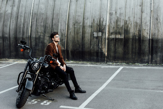 Full Length View Of Handsome Man In Jacket Resting On Black Motorcycle And Looking Away