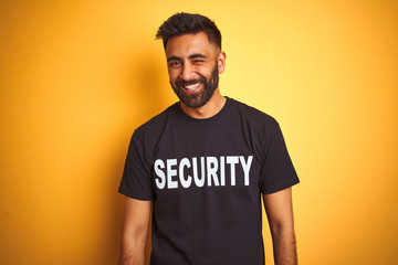 Arab indian hispanic safeguard man wearing security uniform over isolated yellow background winking...