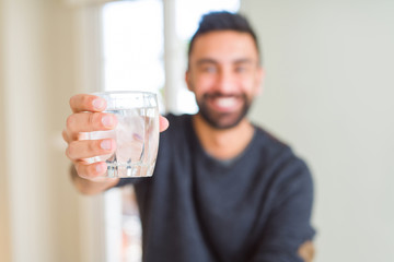 Handsome hispanic man drinking a fresh glass of water with a happy face standing and smiling with a confident smile showing teeth