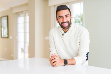Fototapeta premium Handsome hispanic man wearing casual white sweater at home sticking tongue out happy with funny expression. Emotion concept.