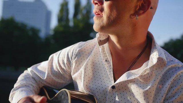Man plays guitar and sings against the lake. Guitarist touching guitar strings. Close up shot.
