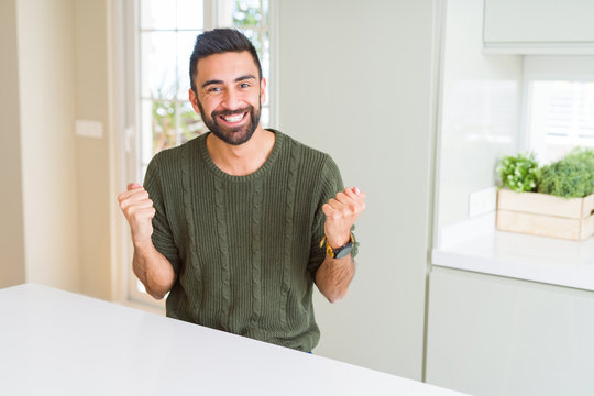 Handsome hispanic man wearing casual sweater at home celebrating surprised and amazed for success with arms raised and open eyes. Winner concept.