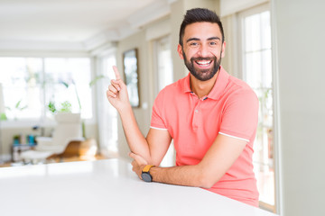 Fototapeta premium Handsome hispanic man wearing casual t-shirt at home with a big smile on face, pointing with hand and finger to the side looking at the camera.