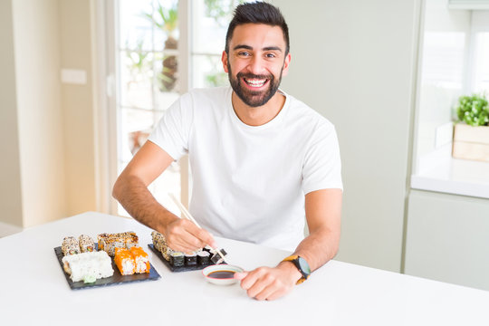 Handsome man smiling happy enjoying eating fresh colorful asian sushi using chopsticks