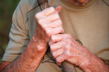 Close up of a very old mans or womans hands are holding an old gnarled stick instead of a cane