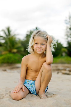 Blond haired boy kneeling on beach