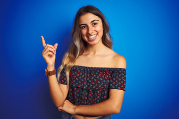 Young beautiful woman wearing floral t-shirt over blue isolated background with a big smile on face, pointing with hand and finger to the side looking at the camera.