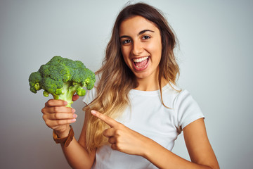 Young beautiful woman eating broccoli over grey isolated background very happy pointing with hand and finger