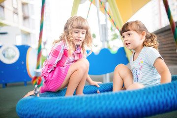Fototapeta na wymiar Two cute happy little girls, kids having fun on swings at playground