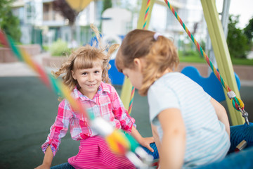 Fototapeta na wymiar Two cute happy little girls, kids having fun on swings at playground