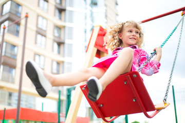 Cute happy little girl, kid having fun on swings at playground