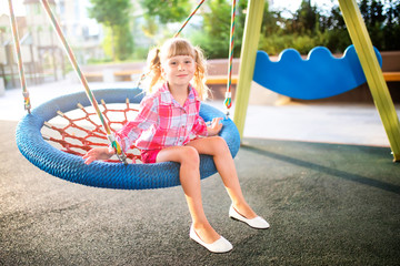 Cute happy little girl, kid having fun on swings at playground