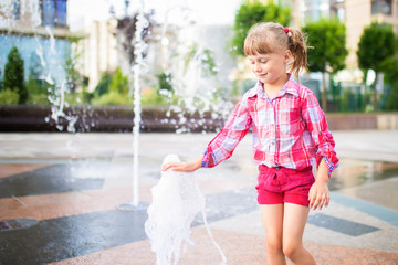 Naklejka premium Little adorable girl having fun in street fountain at hot sunny day