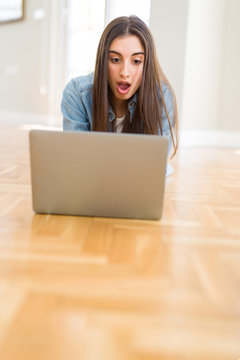 Beautiful young woman laying on the floor using laptop scared in shock with a surprise face, afraid and excited with fear expression