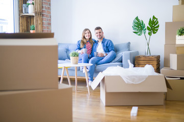 Fototapeta na wymiar Young couple relaxing drinking a cup of coffee sitting at sofa of new home with cardboard boxes around them, very happy moving to a new apartment