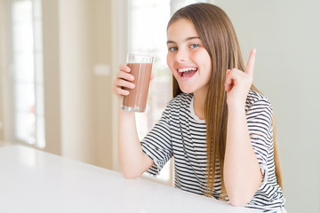 Beautiful young girl kid drinking fresh tasty chocolate milkshake as snack surprised with an idea or question pointing finger with happy face, number one