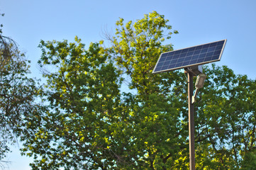 street lamp with a solar battery against a blue sky and trees