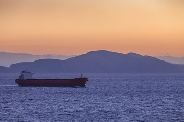 Ship sailing at sunset with island silhouette background