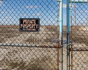 Chain link fence gates chained and locked with no trespassing, private property sign at abandoned...