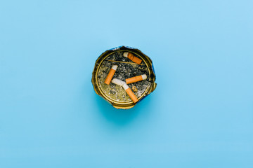 Ashtray with cigarette butts and ash on a blue background. Unfinished cigarettes in an iron can....