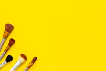 Brushes for make up on yellow visagiste work desk background top view copyspace