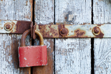 Old brown padlock on a gray door with wooden planks of cracked paint and rust. Vintage gates with...
