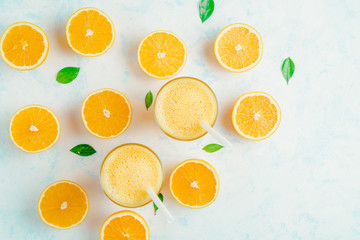 Top view of orange smoothie and orange fruits with green leaves on white background.
