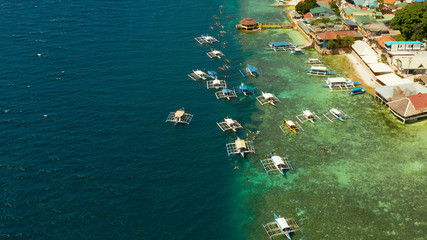 People snorkeling over coral reef with clear blue ocean water, top view. Moalboal, Philippines. People swim in the transparent sea between coral reefs. Summer and travel vacation concept.