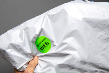 Man hand holding plastic bag parcel with Commande Web sticker translated as internet order