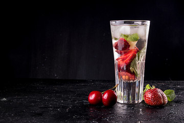 Summer strawberry sweet cherry cocktail ice cold drink in glasses on black background.