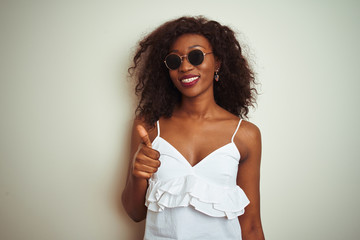 Young african american woman wearing t-shirt and sunglasses over isolated white background doing happy thumbs up gesture with hand. Approving expression looking at the camera with showing success.