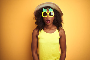 African american woman wearing funny pineapple sunglasses over isolated yellow background afraid and shocked with surprise expression, fear and excited face.