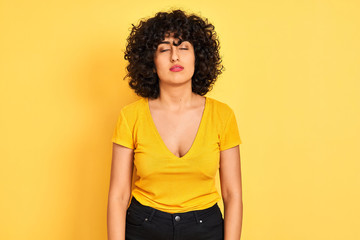Young arab woman with curly hair wearing t-shirt standing over isolated yellow background looking sleepy and tired, exhausted for fatigue and hangover, lazy eyes in the morning.